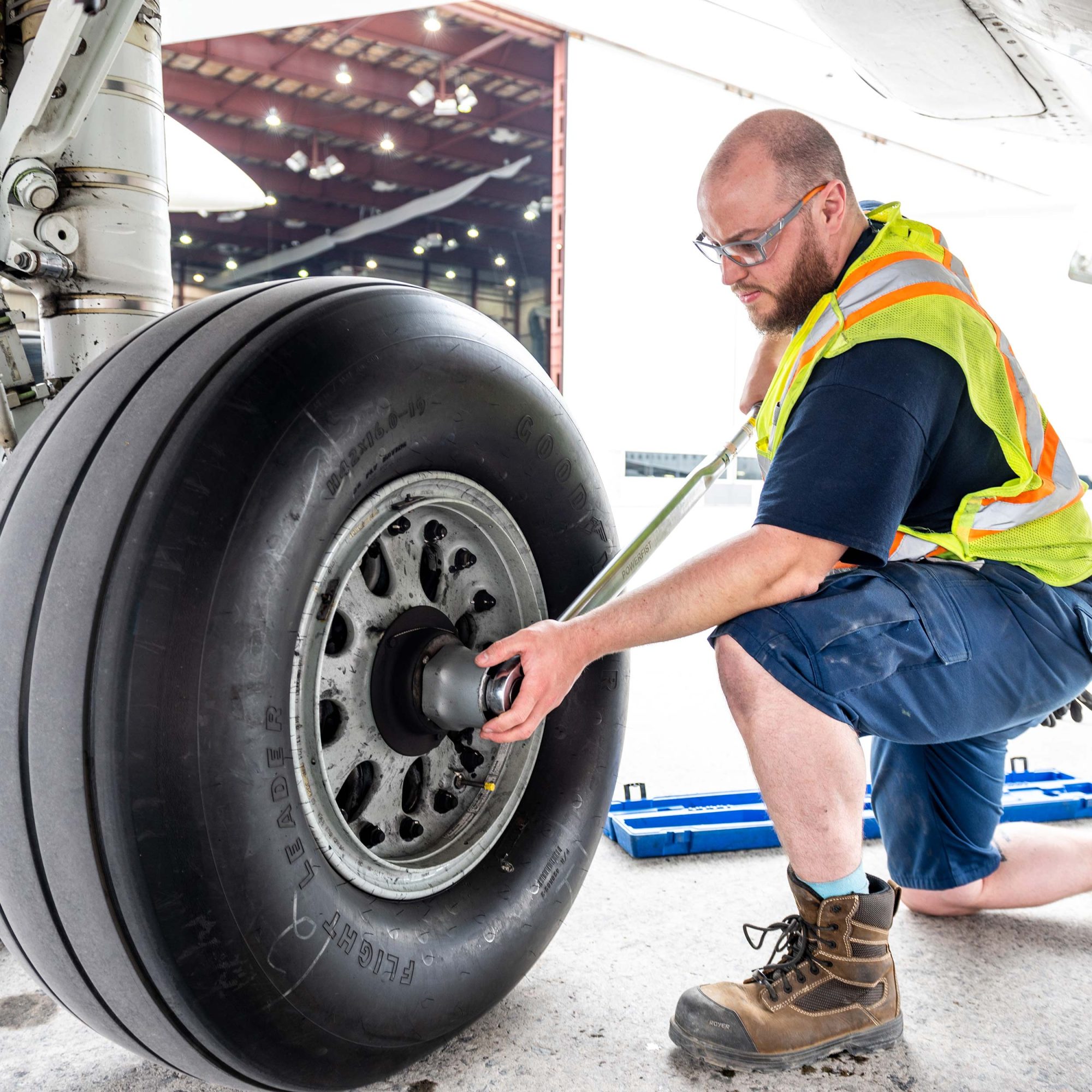 Technicien en gilet de sécurité effectuant l’entretien d’une roue d’avion avec une clé dynamométrique devant un hangar.