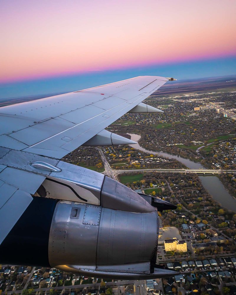 Vue aérienne d’une ville au coucher du soleil depuis le hublot d’un avion, avec l’aile et le moteur en premier plan.