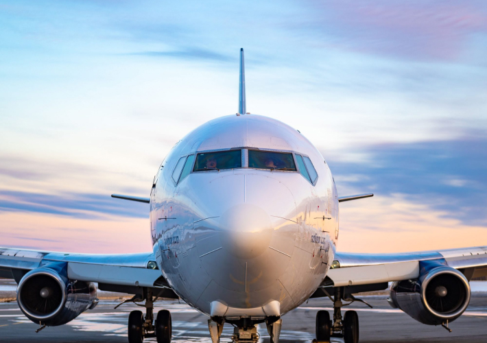 Avion vu de face sur le tarmac au lever ou coucher du soleil, avec un ciel coloré en arrière-plan.
