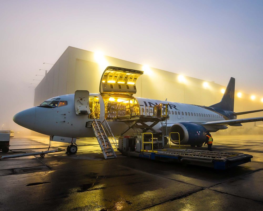 Avion cargo Nolinor au sol dans la brume, portes ouvertes et éclairage intérieur allumé pendant le chargement de marchandises.